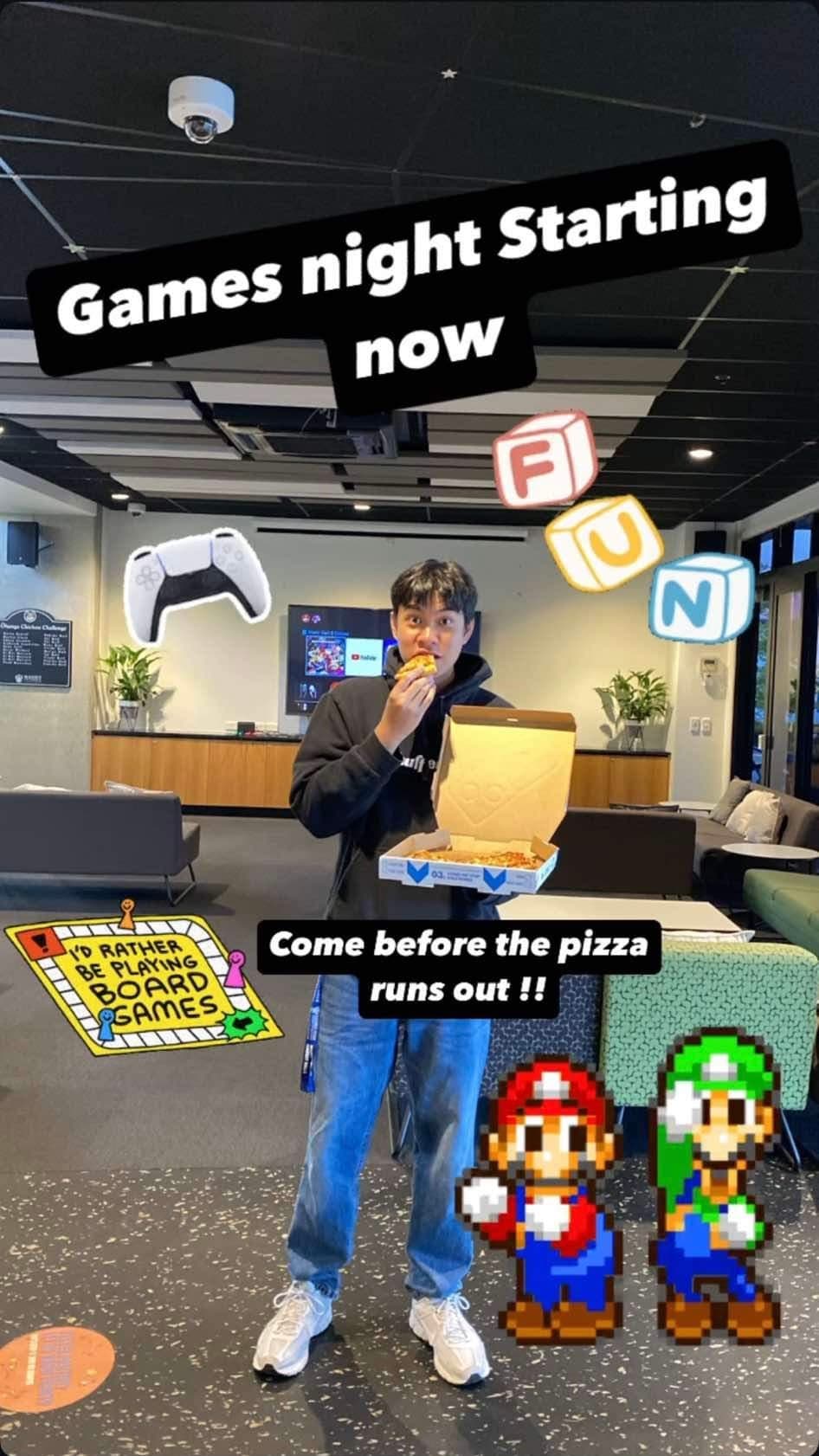 Promoting a games night in the village lounge, holding pizza boxes in front of the consoles and the board game shelf.